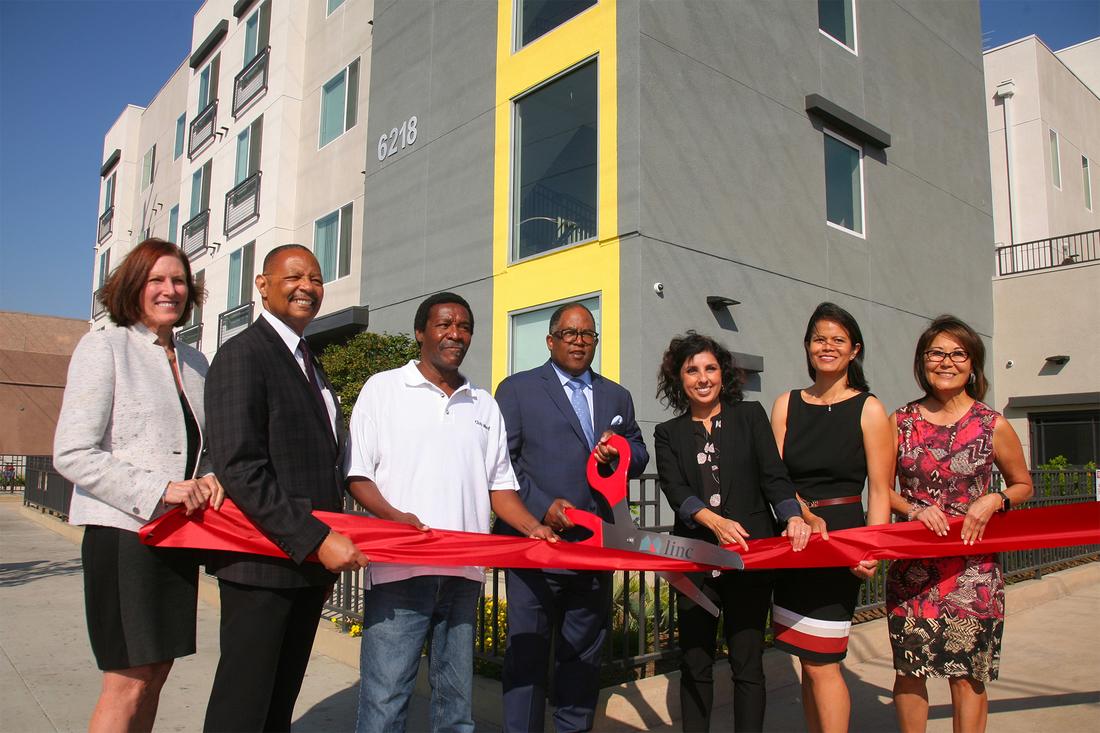 a group of people cutting a ribbon in front of a building.