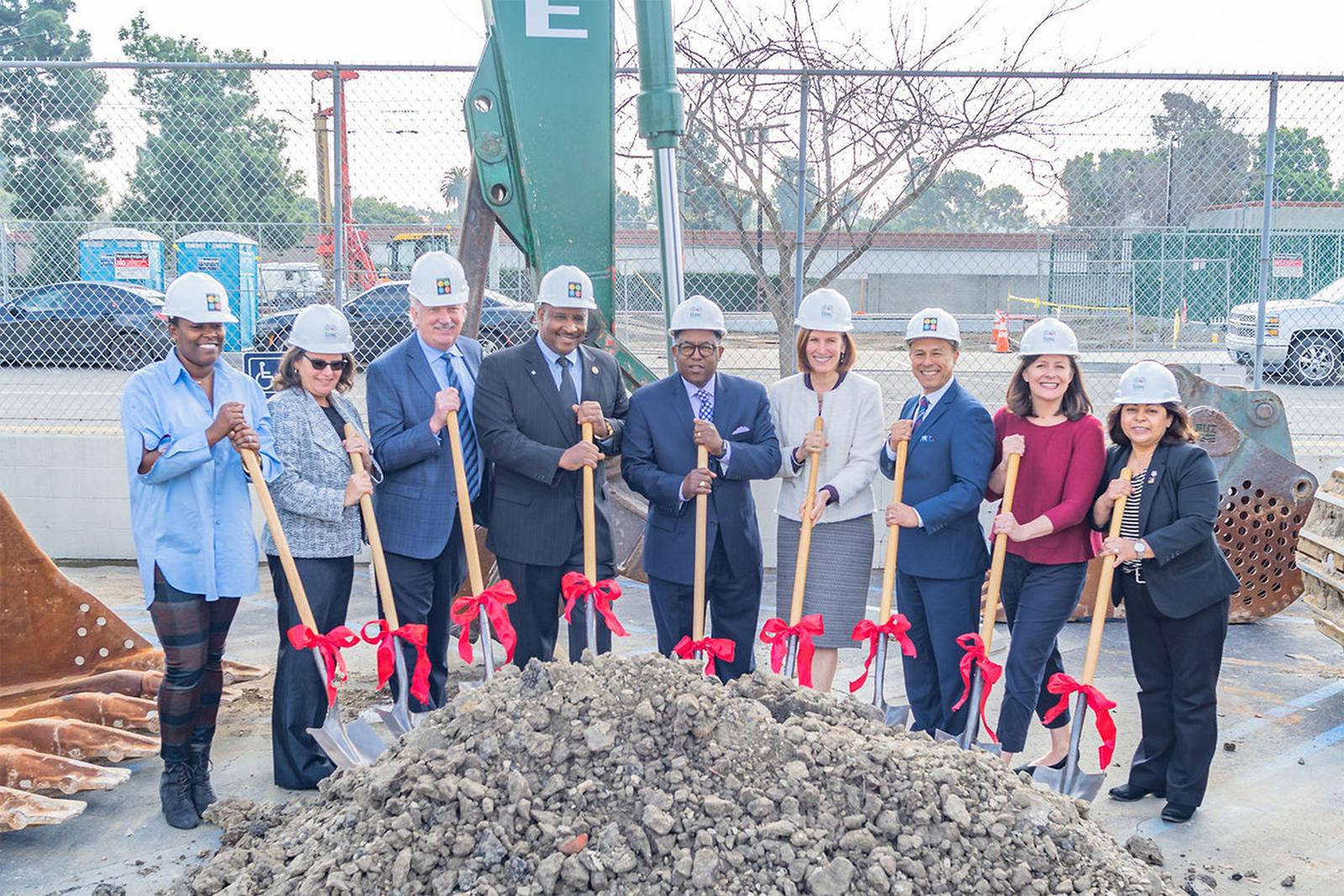 a group of people holding shovels standing next to a pile of dirt.